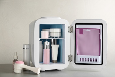 Photo of Open cosmetic refrigerator and skin care products on beige background