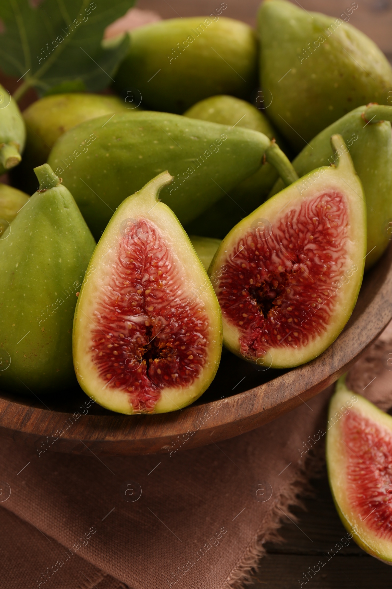 Photo of Cut and whole green figs in bowl on table, closeup