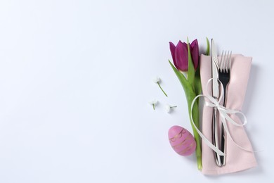 Photo of Cutlery set, Easter egg and tulip on white background, top view with space for text. Festive table setting