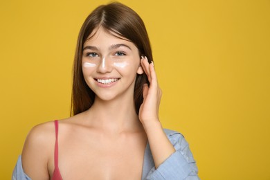 Photo of Teenage girl with sun protection cream on her face against yellow background. Space for text