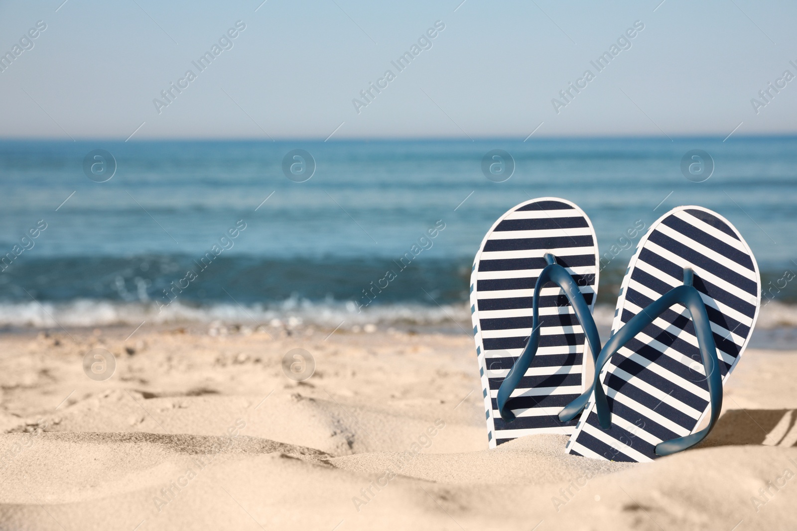 Photo of Stylish flip flops in sand on beach. Space for text