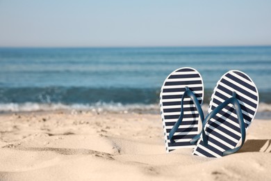 Stylish flip flops in sand on beach. Space for text