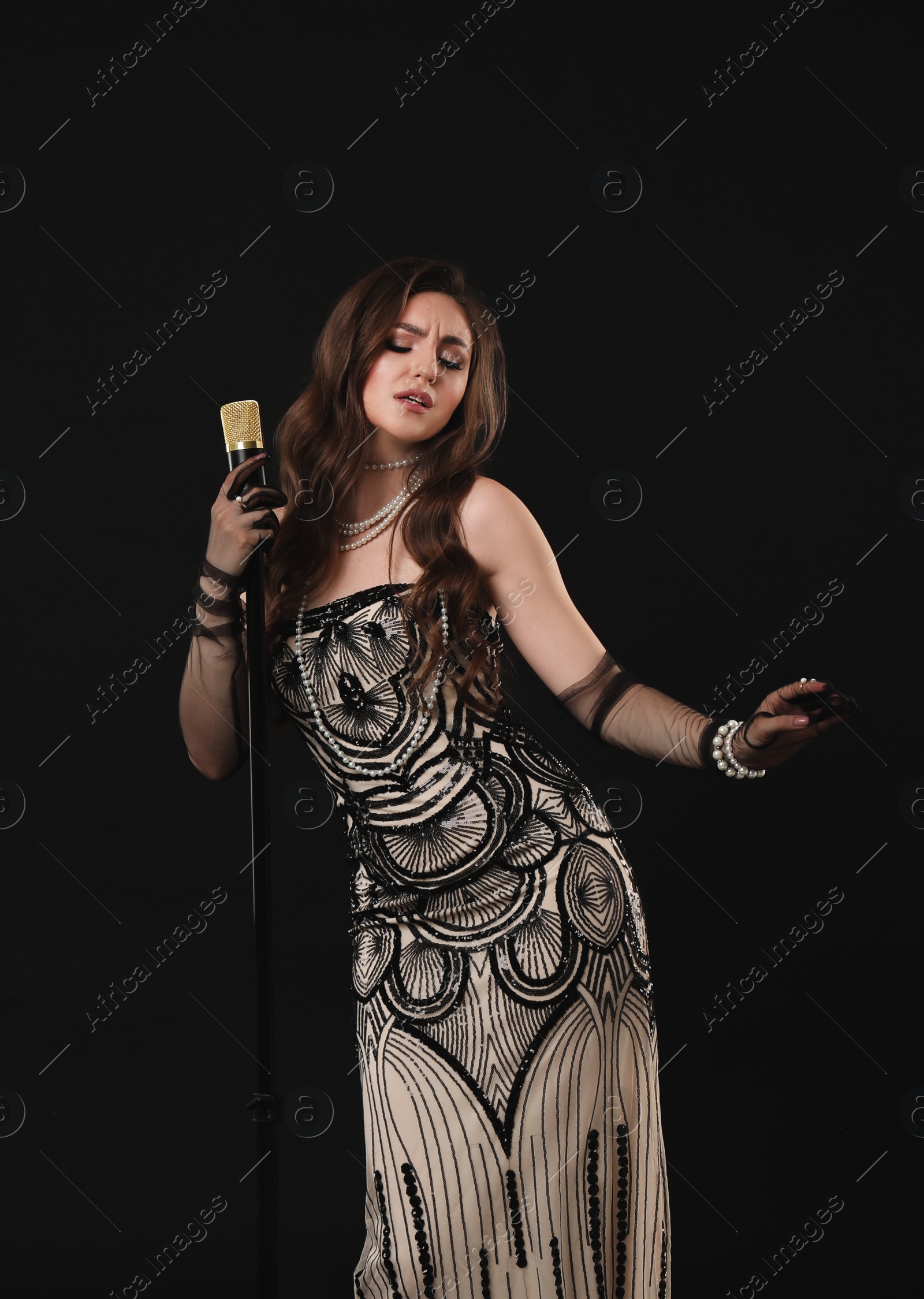 Photo of Beautiful young woman in stylish dress with microphone singing on black background