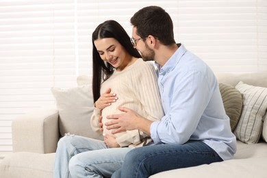 Happy pregnant woman spending time with her husband on sofa at home