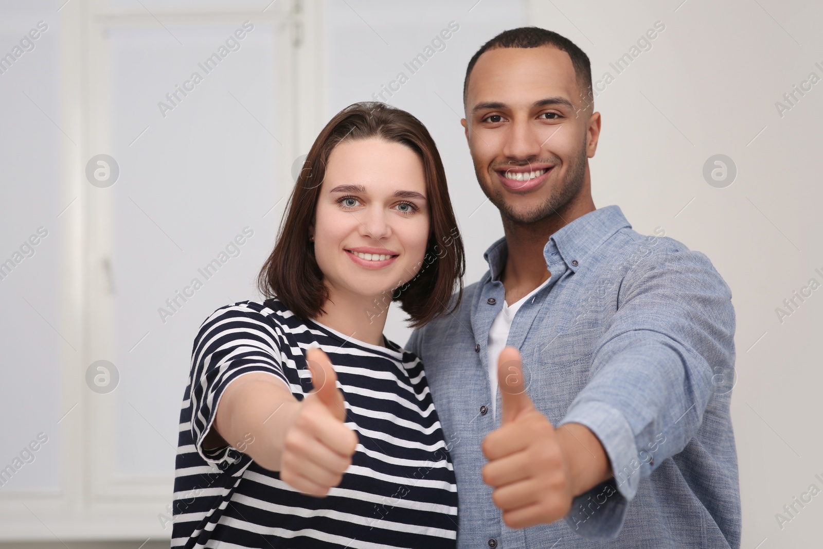 Photo of Dating agency. Happy couple showing thumbs up near white wall