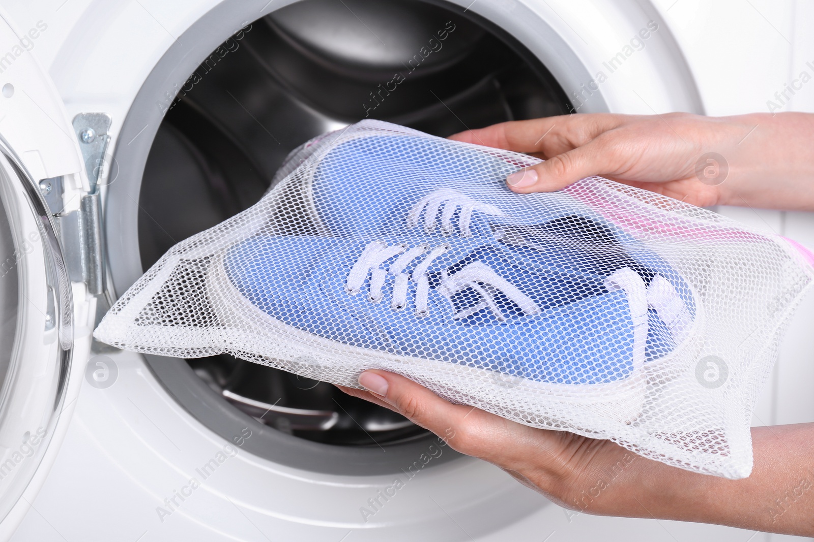 Photo of Woman putting pair of sport shoes in mesh laundry bag into washing machine, closeup