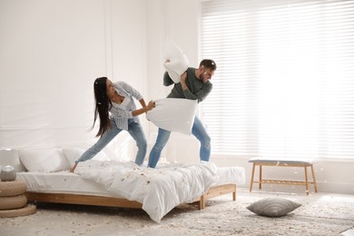 Happy young couple having fun pillow fight in bedroom