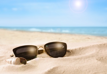 Shell and stylish sunglasses on sandy beach near sea