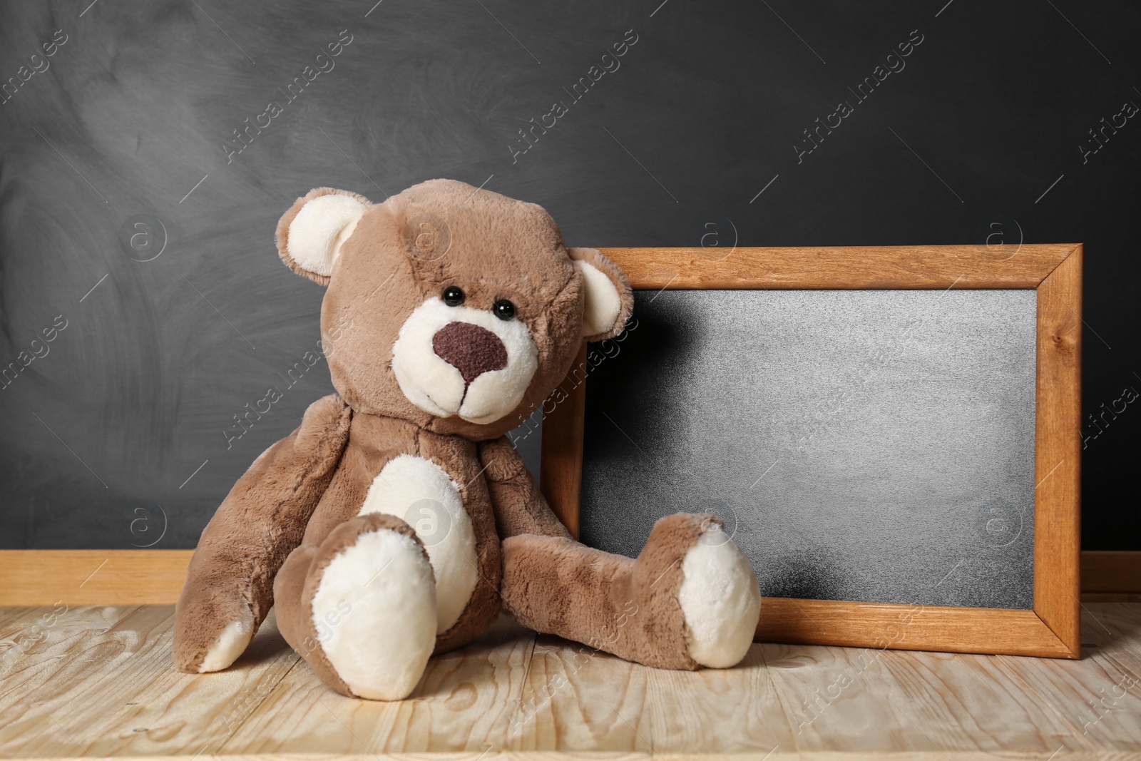 Photo of Teddy bear and small blackboard on wooden table. Space for text