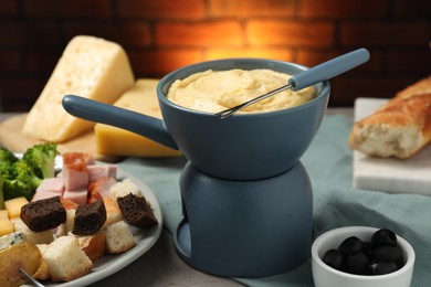 Tasty melted cheese in fondue pot, fork and snacks on table, closeup