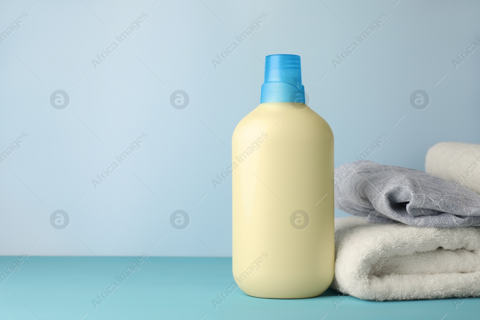 Photo of Bottle of fabric softener and towels on light blue table, space for text