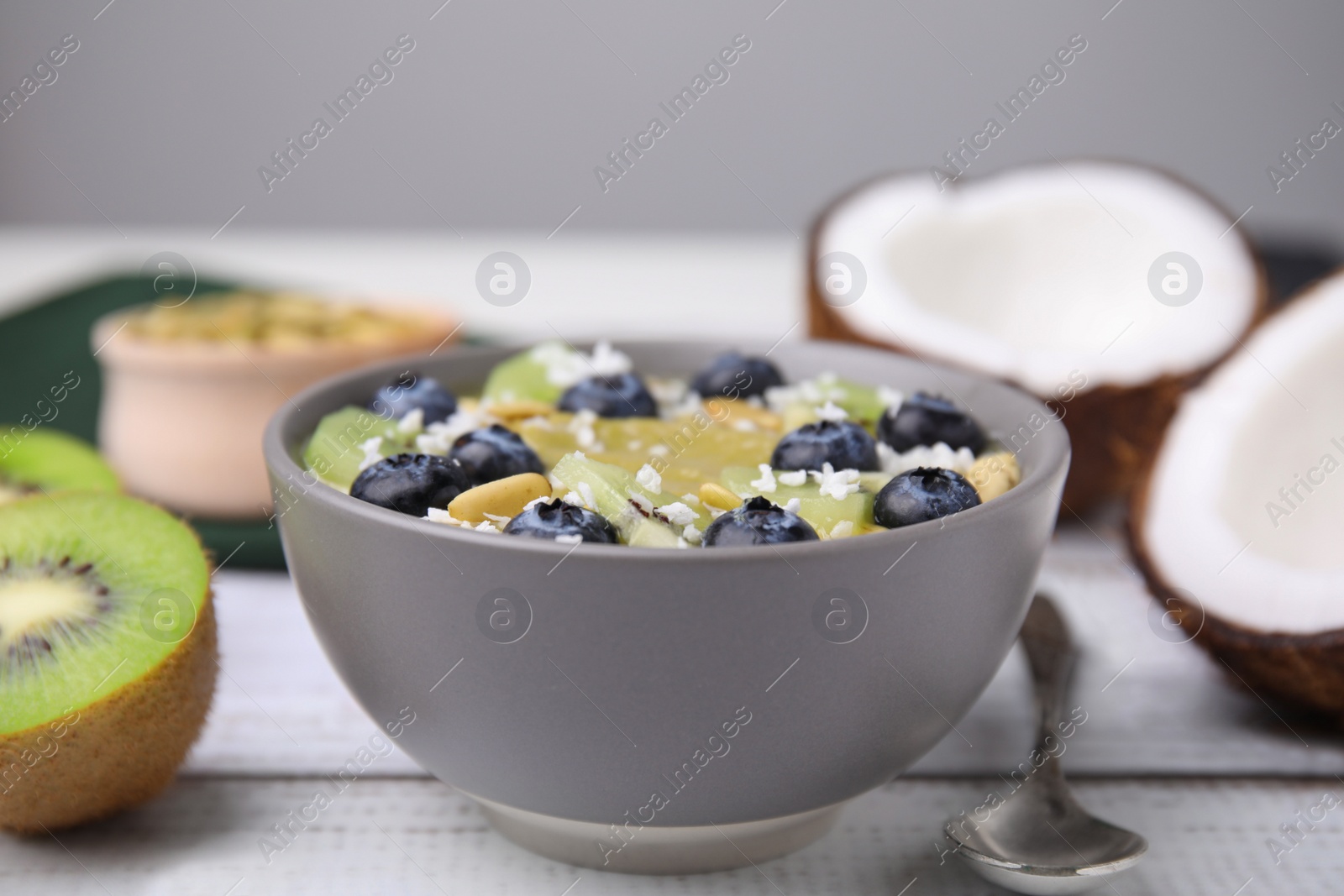 Photo of Bowl of delicious fruit smoothie served with fresh blueberries, kiwi slices and coconut flakes on white wooden table, closeup