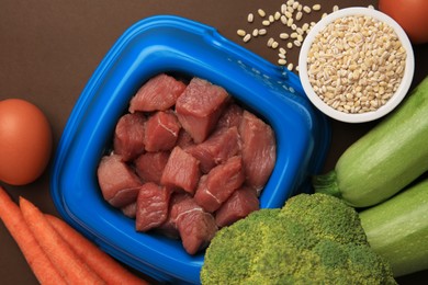 Photo of Raw meat in bowl and healthy products for pet on brown background, flat lay