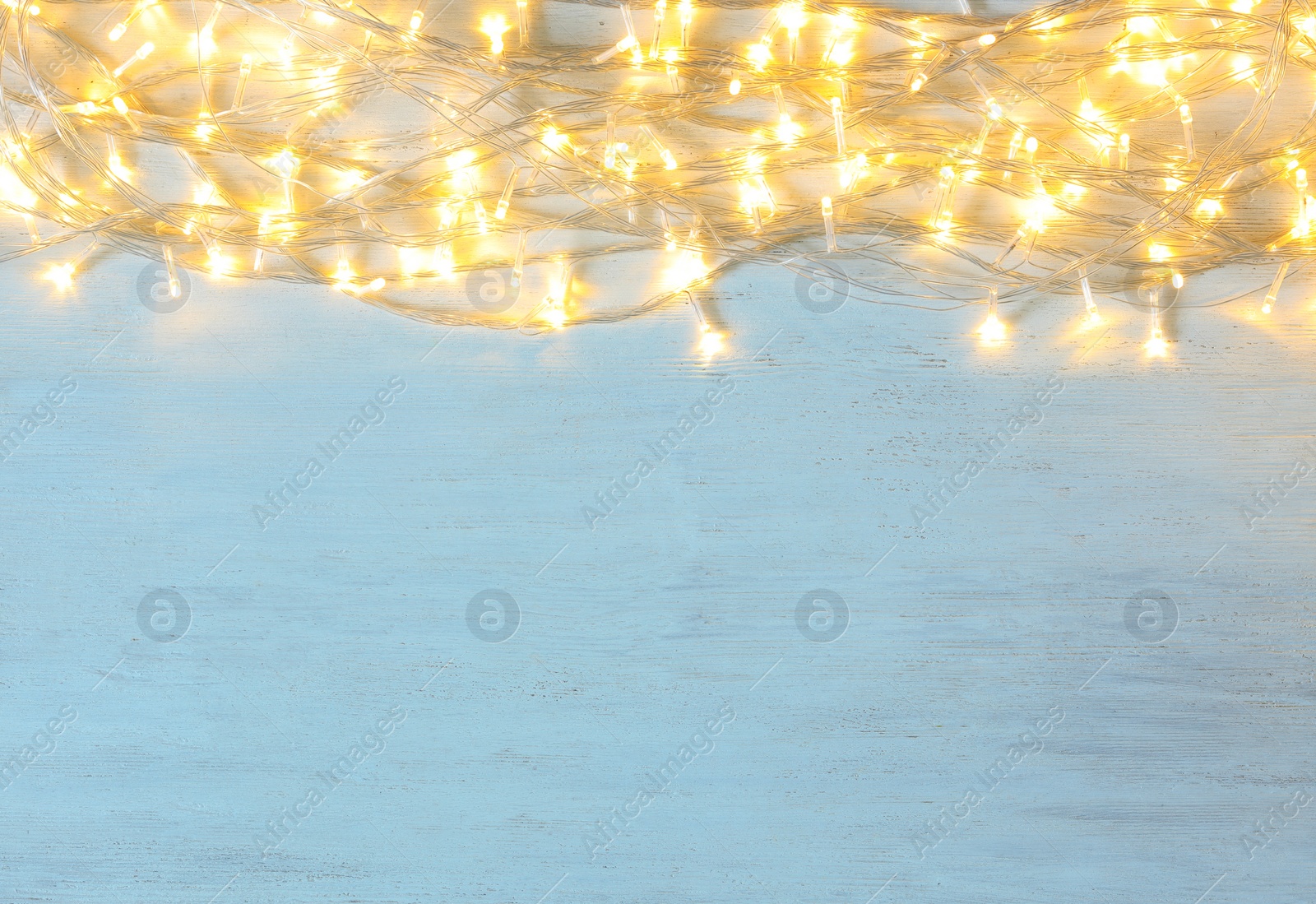 Photo of Christmas lights on light wooden background, top view. Space for text