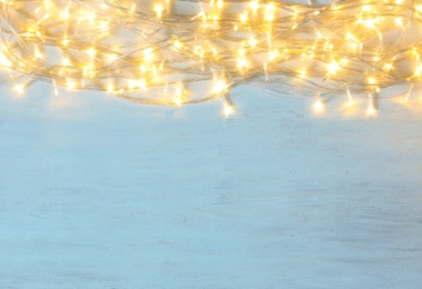 Christmas lights on light wooden background, top view. Space for text