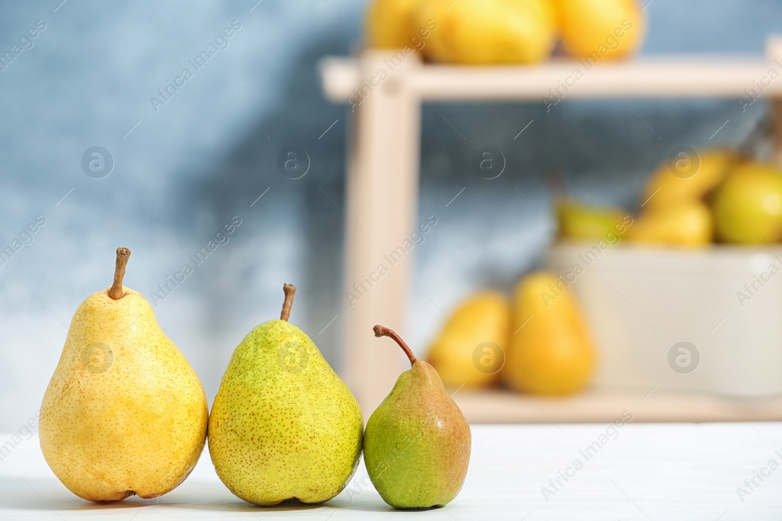 Photo of Fresh ripe pears on light table against blurred background. Space for text