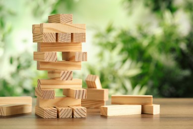 Photo of Jenga tower made of wooden blocks on table outdoors, space for text