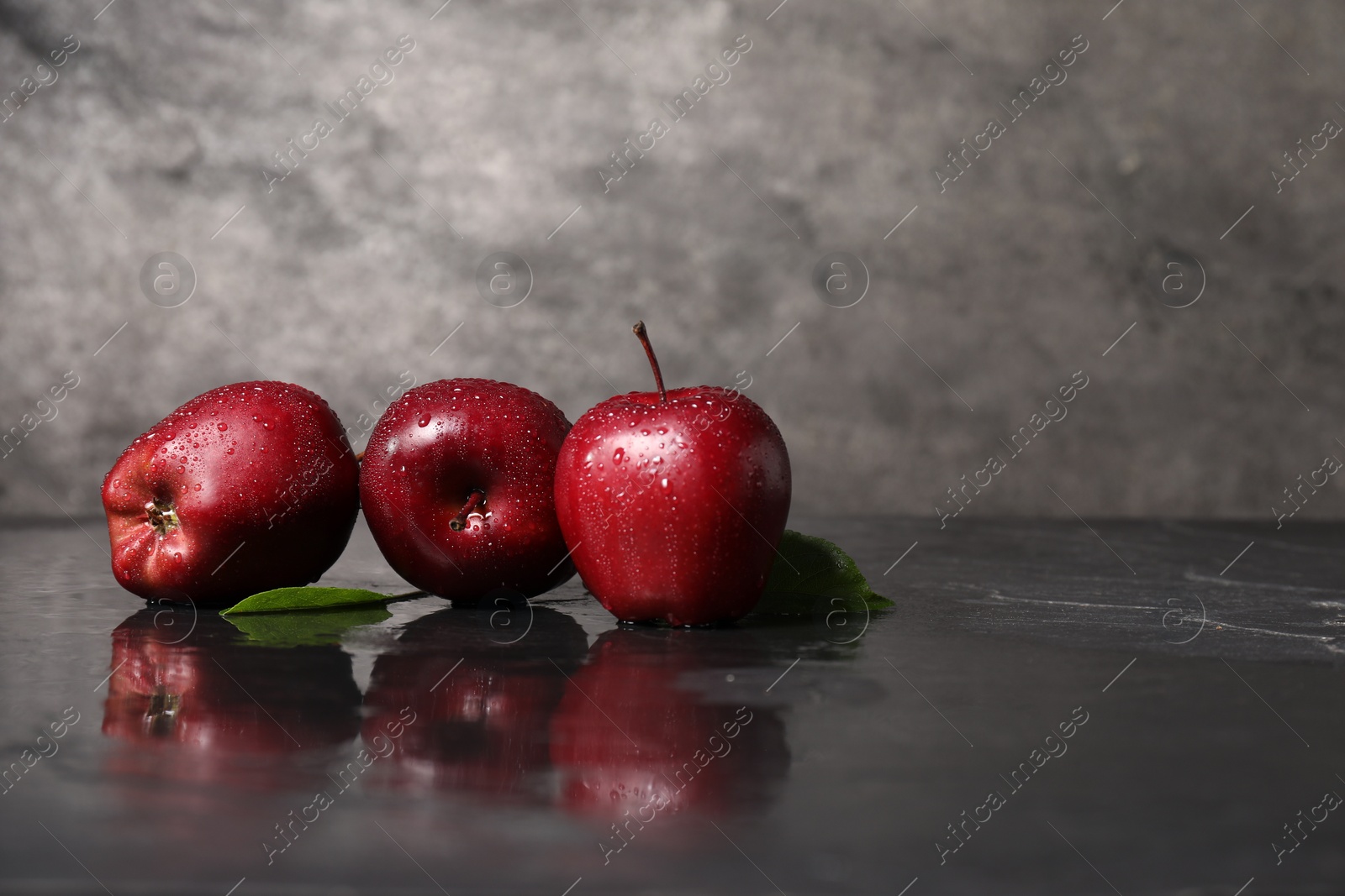 Photo of Wet red apples on dark grey table. Space for text