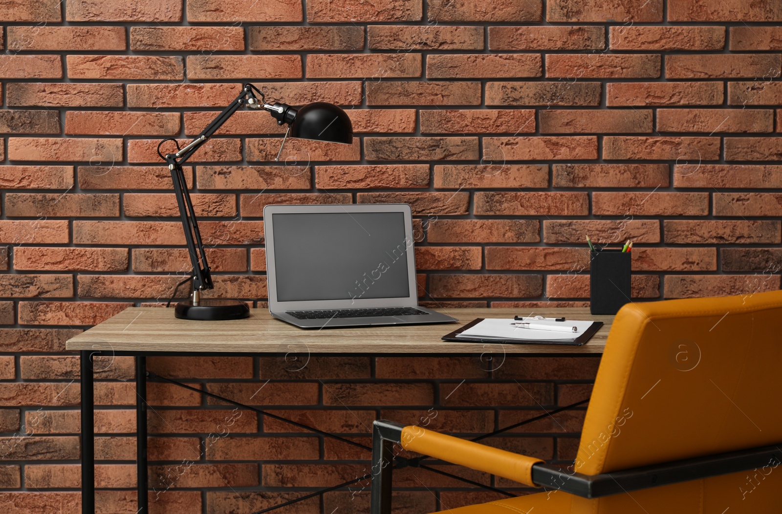 Photo of Stylish workplace with laptop and comfortable chair near brick wall. Interior design