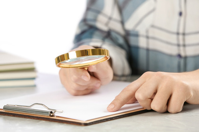 Woman using magnifying glass at table, closeup