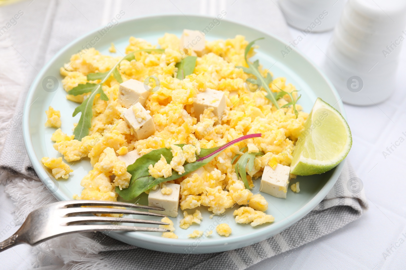 Photo of Delicious scrambled eggs with tofu and lime served on white table, closeup