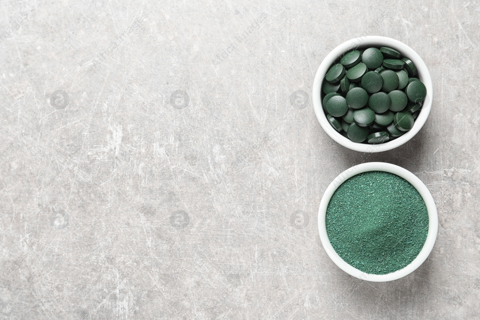 Photo of Bowls of spirulina pills and powder on color background, top view. Space for text