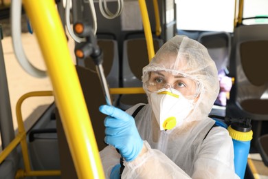 Photo of Public transport sanitation. Worker in protective suit disinfecting bus salon