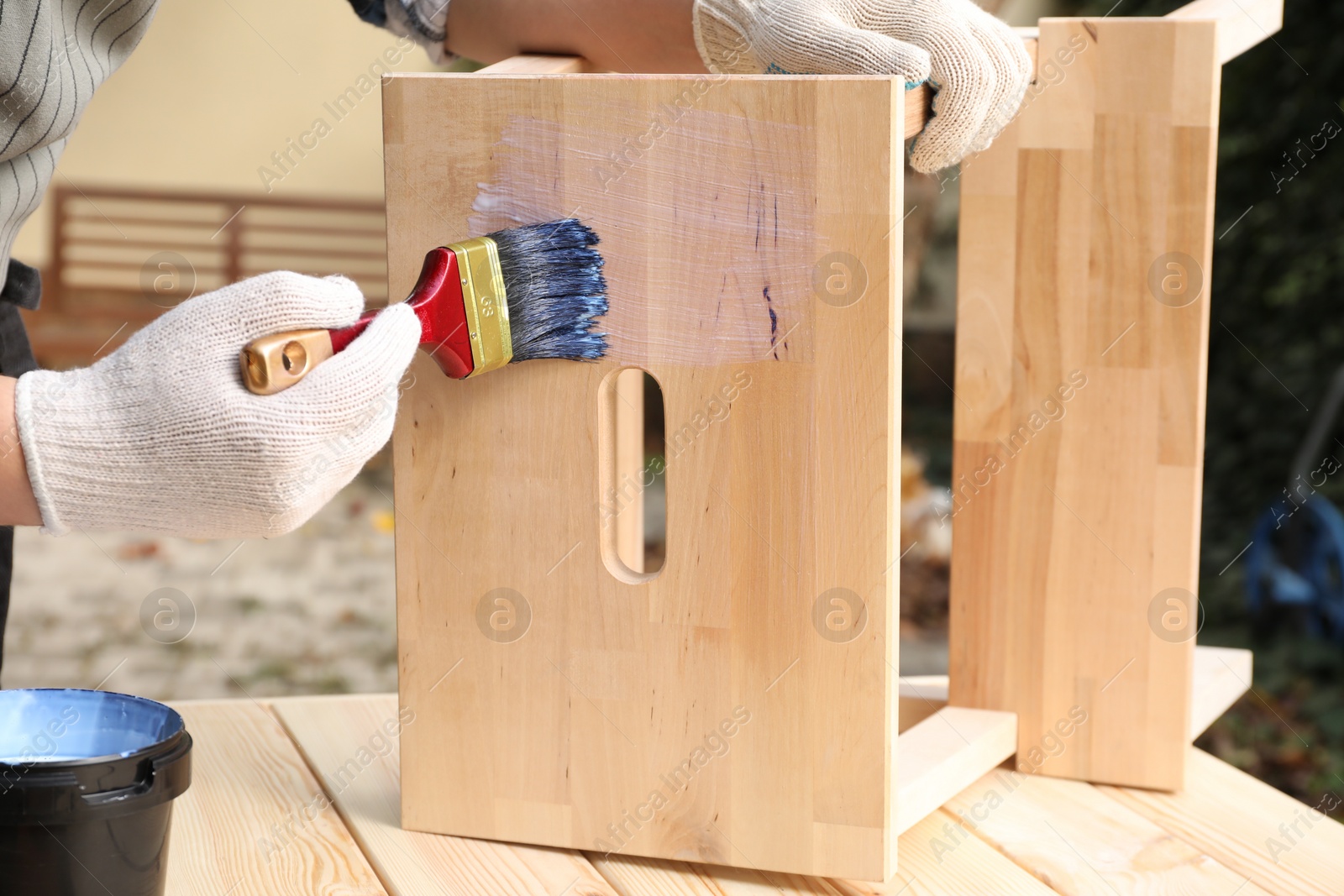 Photo of Man varnishing wooden step stool at table outdoors, closeup