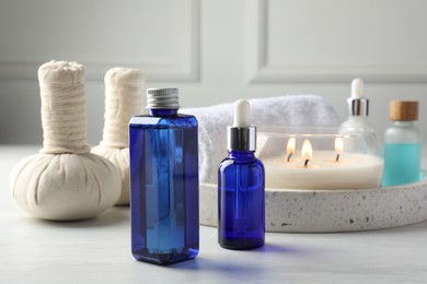 Photo of Spa composition. Bottles of cosmetic products, herbal bags, towel and burning candle on light table