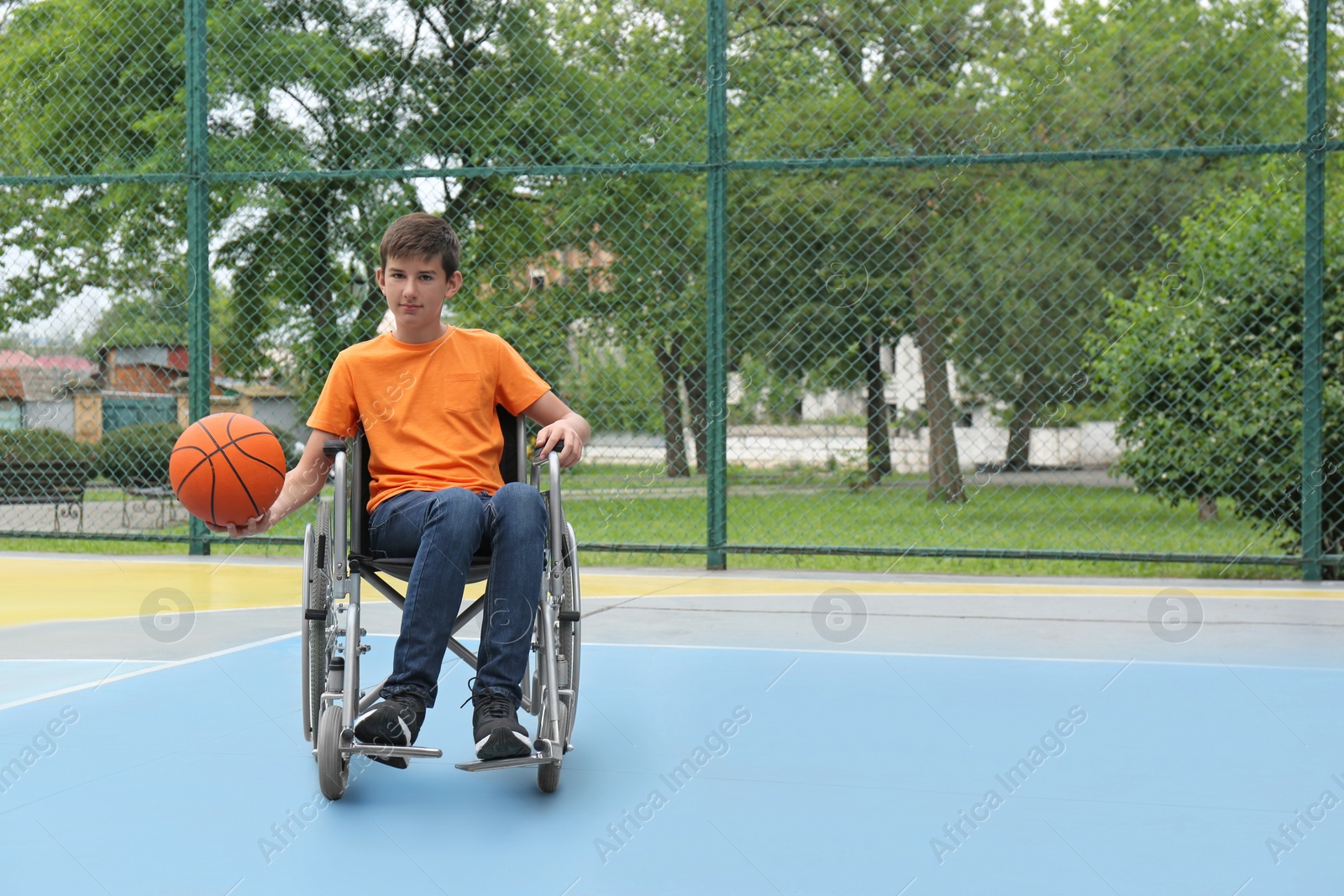 Photo of Disabled teenage boy in wheelchair playing basketball  on outdoor court