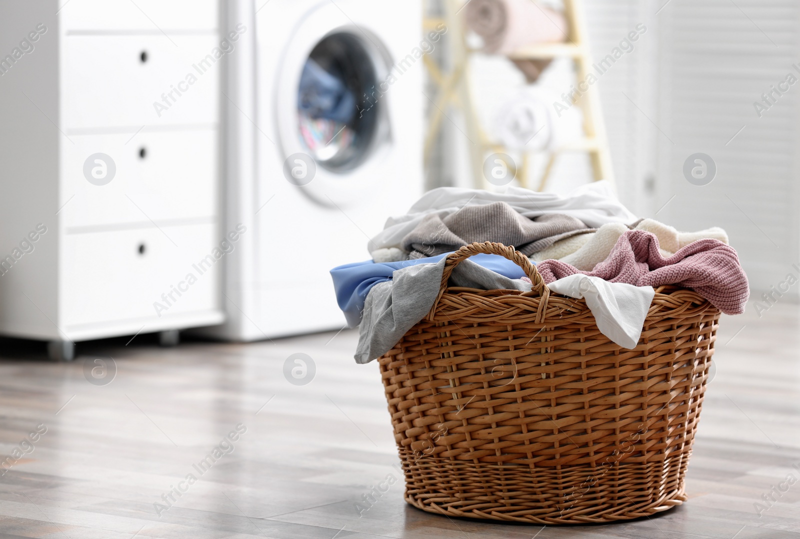 Photo of Wicker basket with dirty laundry on floor indoors, space for text