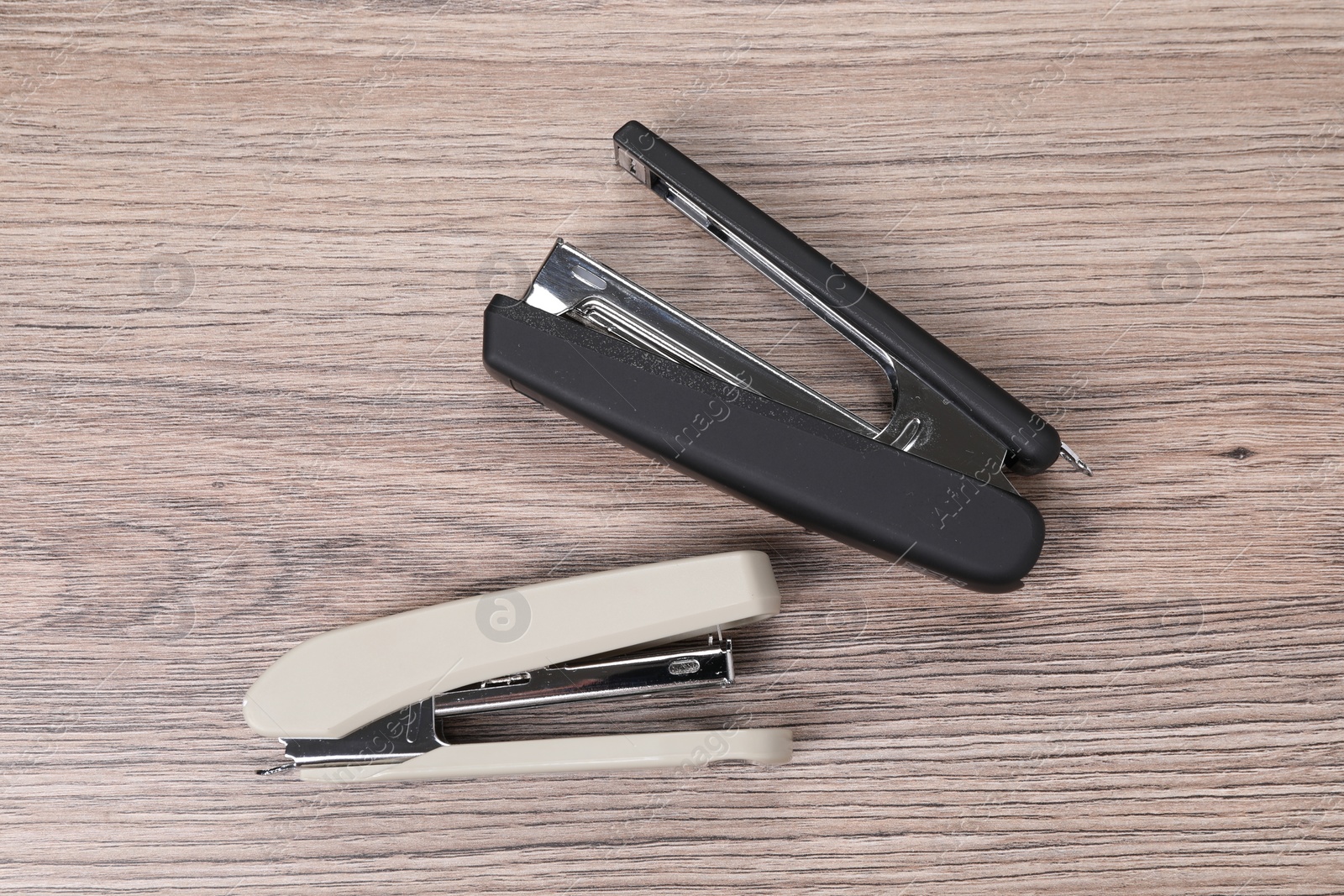 Photo of Black and beige staplers on wooden table, top view