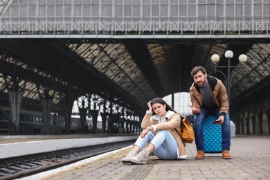 Photo of Being late. Worried couple with suitcase waiting at train station, space for text