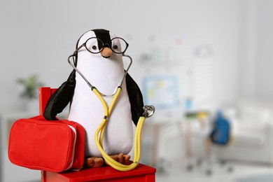 Image of Toy penguin with eyeglasses, stethoscope and first aid bag indoors, space for text. Pediatrician practice