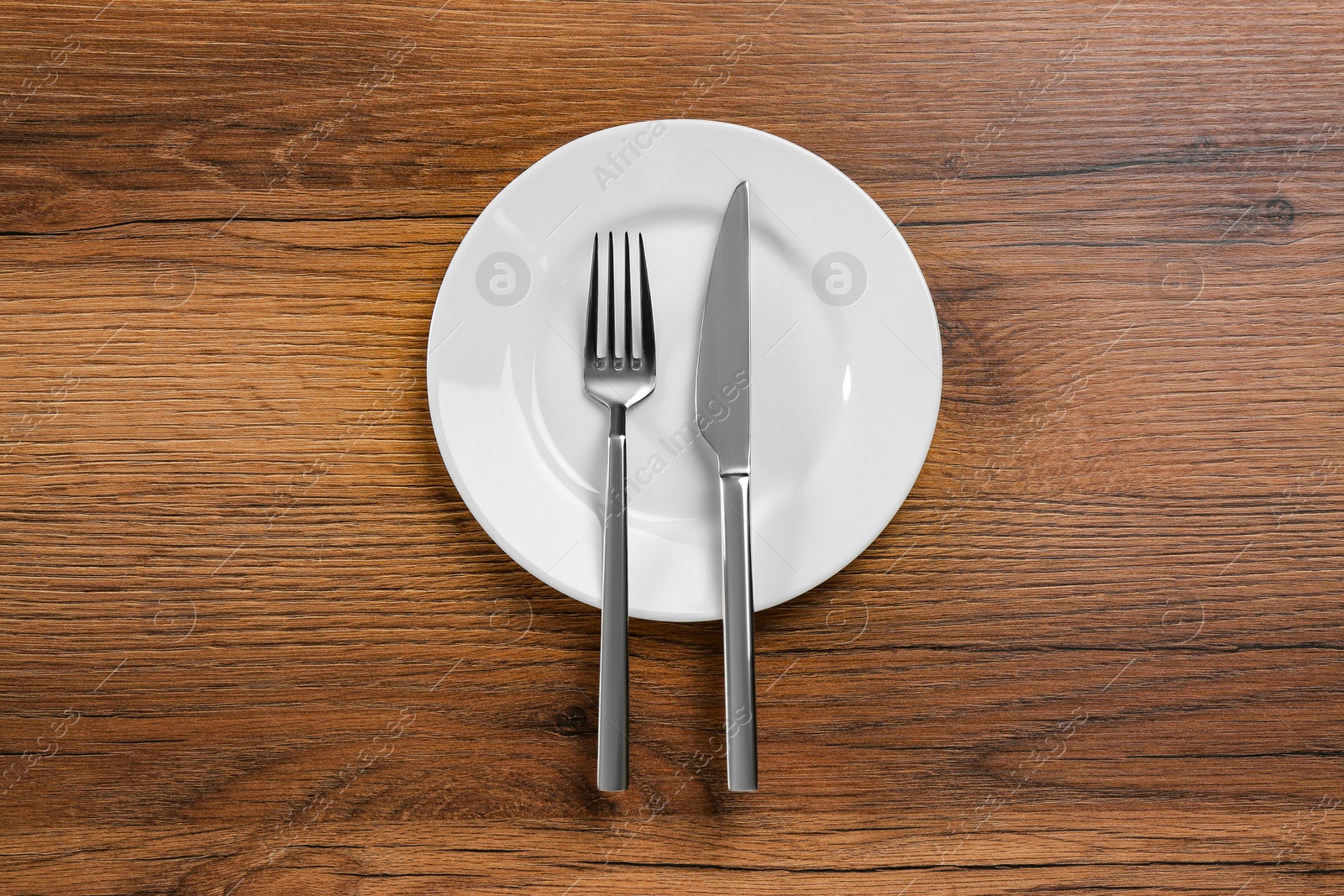 Photo of White plate, fork and knife on wooden table, top view