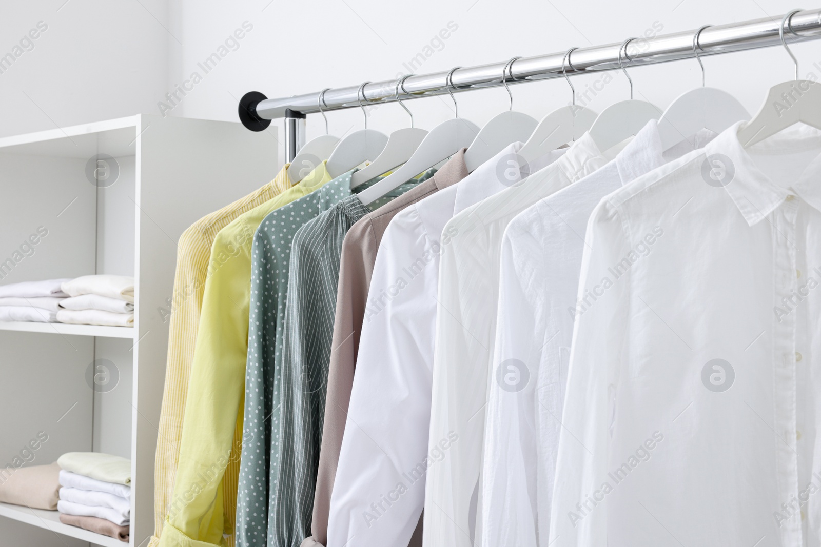 Photo of Wardrobe organization. Rack with different stylish clothes near white wall, closeup