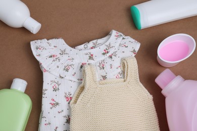 Photo of Laundry detergents and baby clothes on brown background, flat lay