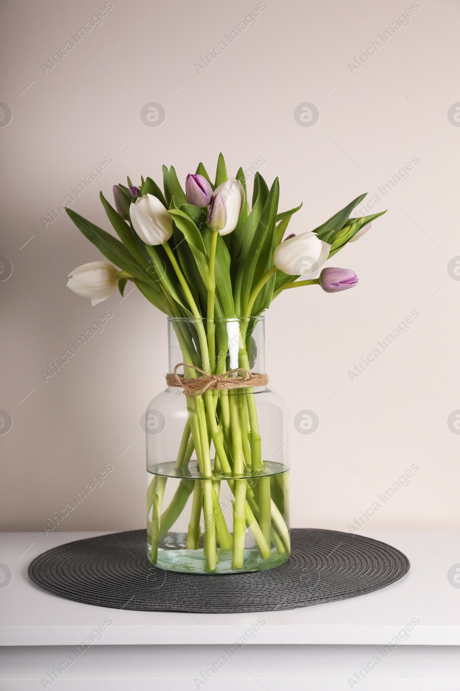 Photo of Beautiful bouquet of colorful tulips in glass vase on table against pink background