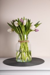 Beautiful bouquet of colorful tulips in glass vase on table against pink background