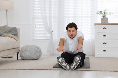 Overweight man stretching on mat at home, space for text