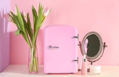 Photo of Cosmetic refrigerator and skin care products on color background