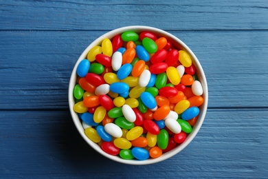 Photo of Bowl with colorful jelly beans on blue wooden background, top view