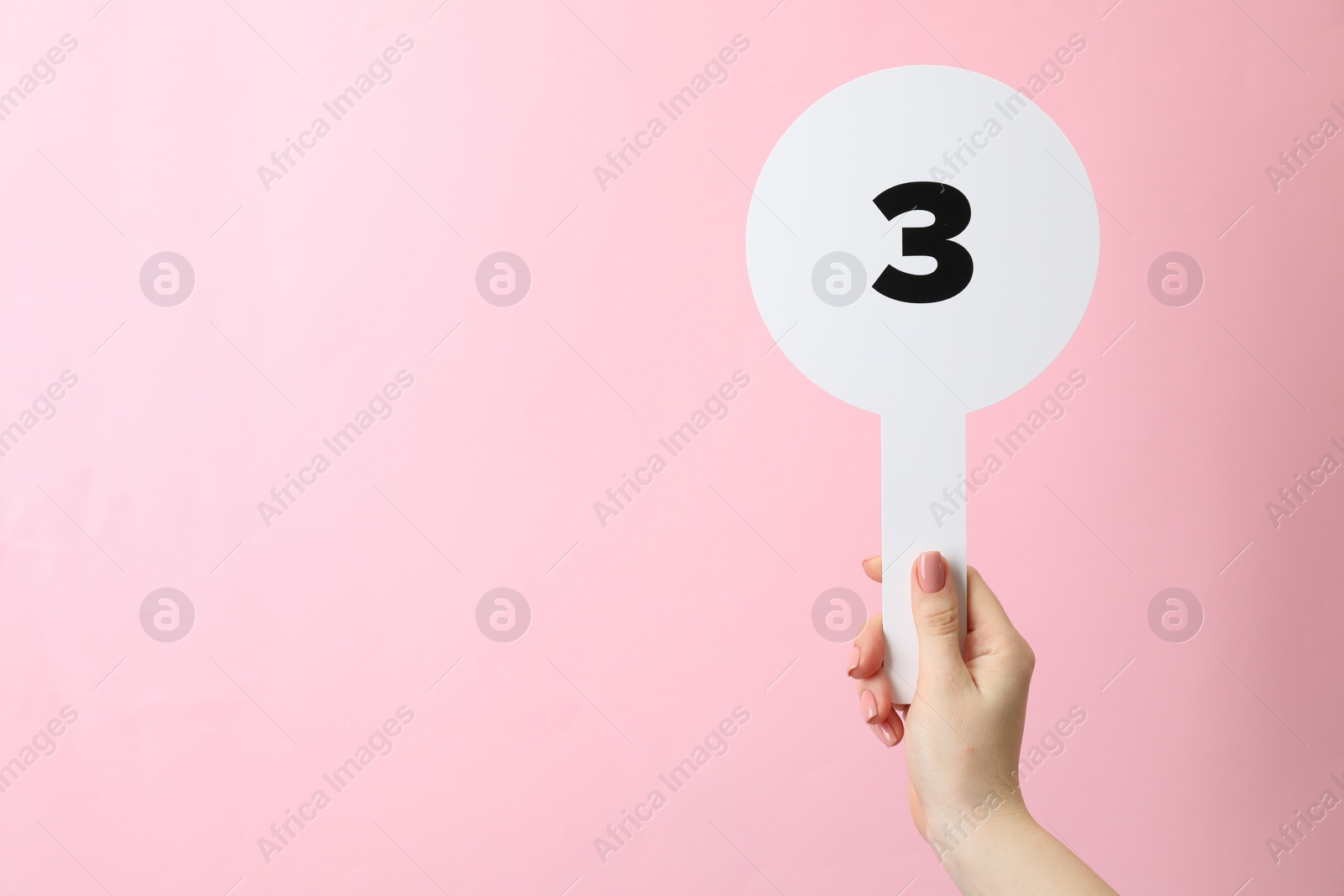 Photo of Woman holding auction paddle with number 3 on pink background, closeup. Space for text