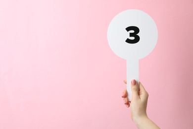 Photo of Woman holding auction paddle with number 3 on pink background, closeup. Space for text