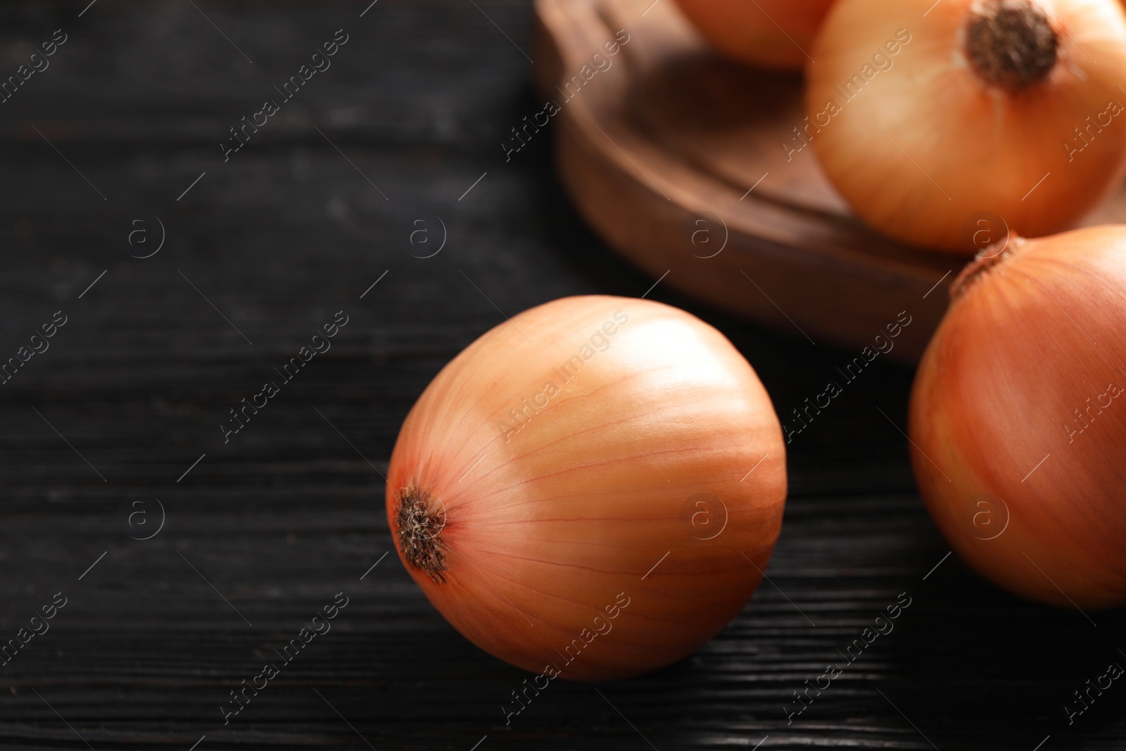 Photo of Ripe onions on black wooden table, closeup