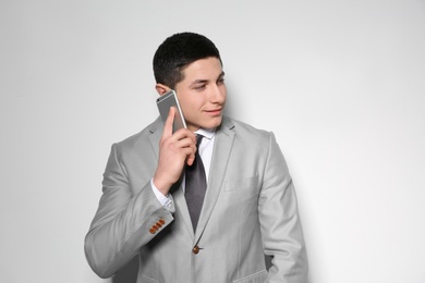 Portrait of young businessman talking on phone against light background