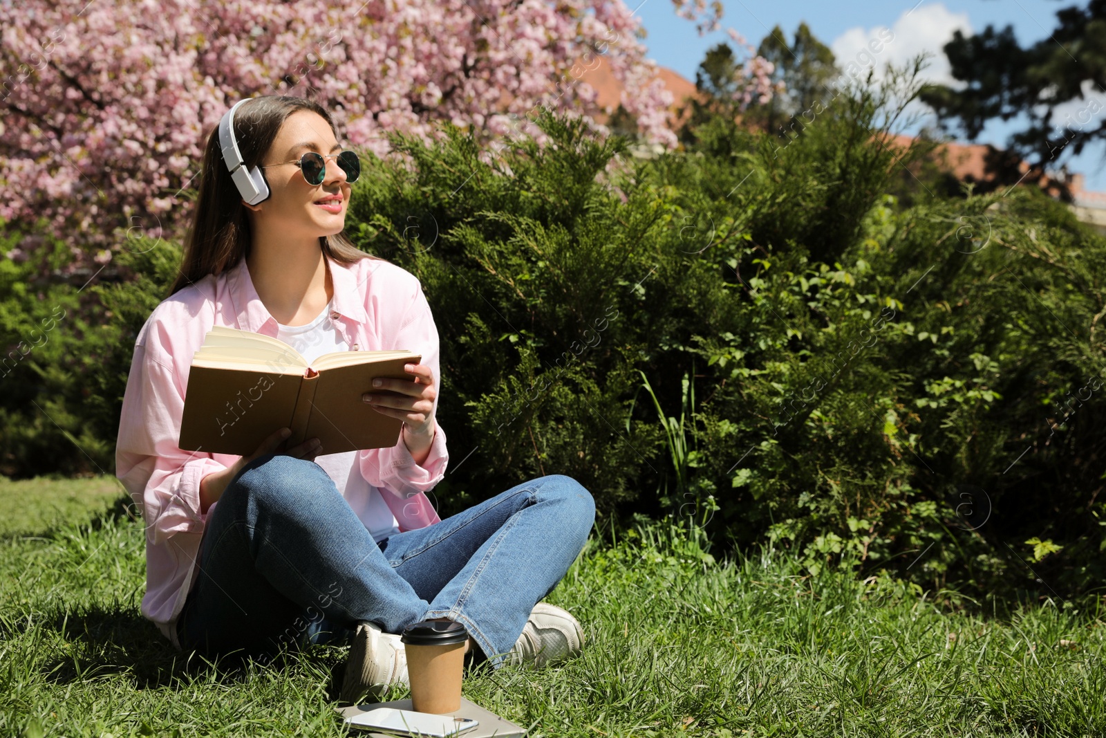 Photo of Happy young woman reading book in park. Space for text