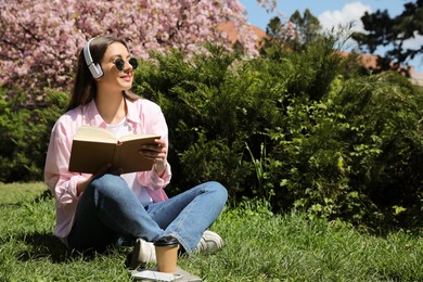 Happy young woman reading book in park. Space for text