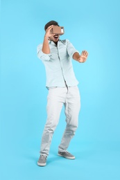 Young man using cardboard virtual reality headset on color background