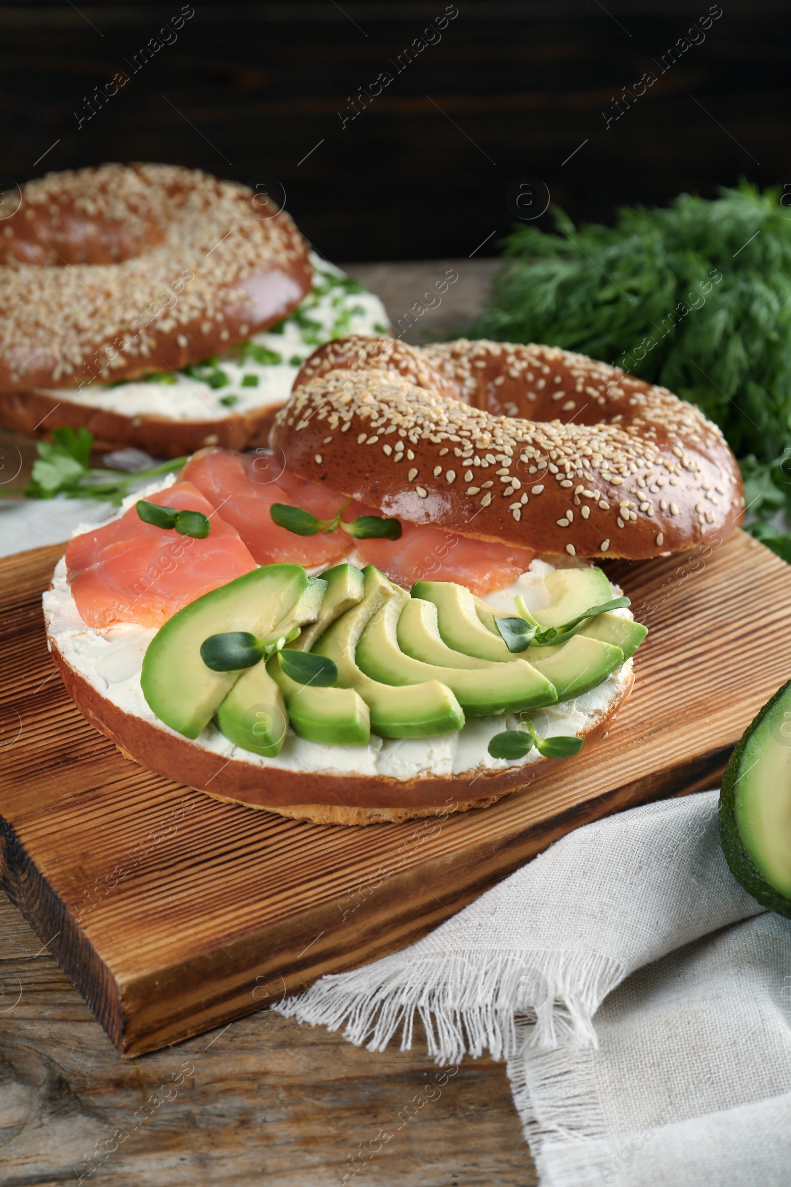 Photo of Delicious bagel with cream cheese, salmon, avocado and microgreens on wooden table